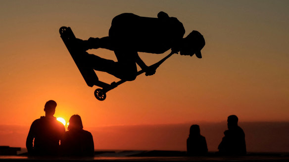 A young man performs a trick on a scooter during the sunset at a skate park on the sea wall of Calais, France.