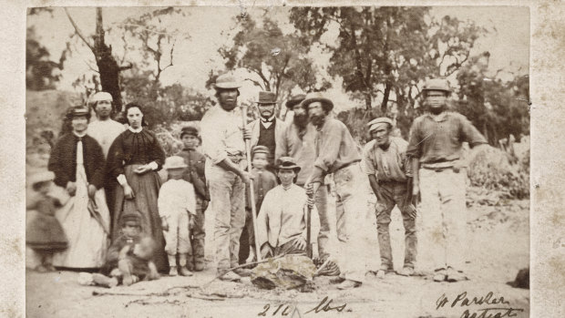 A photo of the Welcome Stranger nuugget finders John Deason (holding crowbar) and Richard Oates (front right, holding tool), friends and family, with quartz standing in for the nugget. Thought to be taken in 1869, a few days after the discovery.