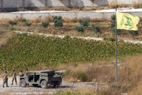 Lebanese soldiers patrol in southern Lebanon next to a Hezbollah flag.