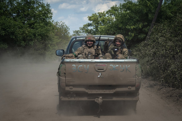 Ukrainian soldiers smile as they get into a pickup van on the front line near Bakhmut.