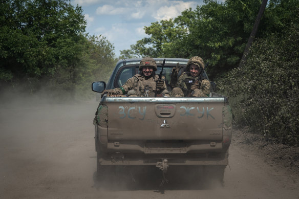 Ukrainian soldiers smile as they ride in a pickup van on the frontline near Bakhmut.