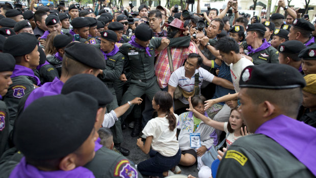 Thai police officers scuffle with pro-democracy supporters and journalist and surround pro-democracy leaders Nuttaa Mahattana, seated with her hands, raised on Tuesday.