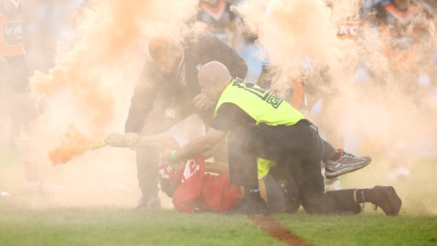 A political protester with a flare is tackled to the ground by security after invading the pitch.
