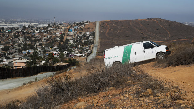 A US Border Patrol van drives up the hill on the US side to pick up migrants apprehended trying to cross from Mexico, left, illegally. 