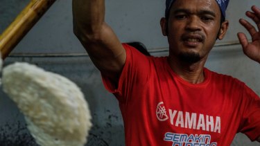 Seorang pria Indonesia memanggang krupuk, kerupuk nasi yang disajikan dengan beberapa hidangan.