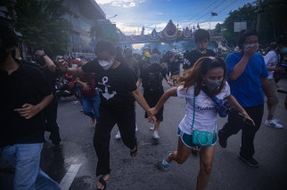 Defying a ban on gatherings imposed due to the COVID-19 outbreak, protesters run from tear gas fired by riot police in Bangkok on Sunday.