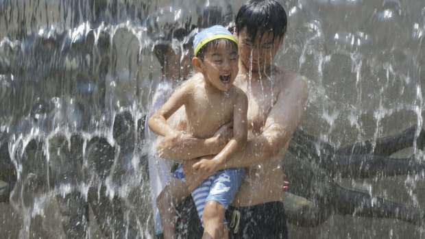 A man holds a child at a water fall to cool off at a park in Tokyo, Monday.