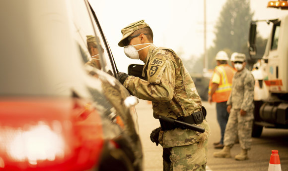 A National Guard specialist from the US Army speaks to a driver at a checkpoint as the Carr fire burns in nearby Redding, California on Saturday.