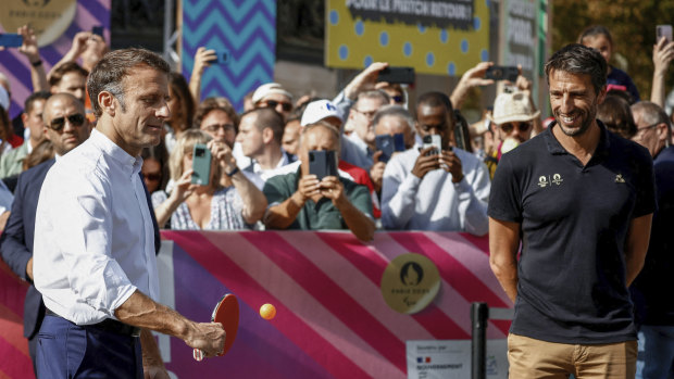 French President Emmanuel Macron plays table tennis as Tony Estanguet, president of the Paris Olympics organizing committee, watches a pre-Games event in Paris.