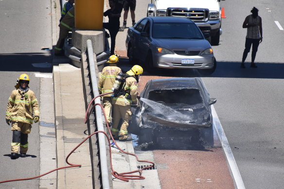 Firefighters extinguish the burnt-out car on the side of the Mitchell Freeway.