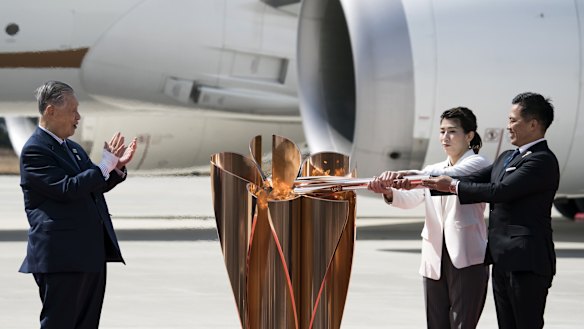 Tokyo Olympic and Paralympic Organising Committee president Yoshiro Mori claps as Olympic gold medalists Tadahiro Nomura, right, and Saori Yoshida, centre, light the Olympic flame.