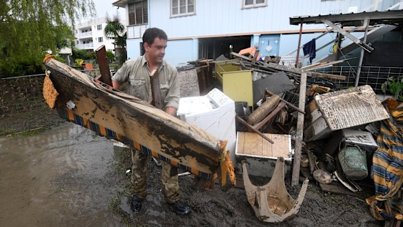 A man helps strangers remove flood-damaged items from their home in the Townsville suburb of Rosslea on Thursday.