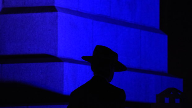 The silhouette of a slouch hat stands out against the blue light projected on the State War Memorial. 