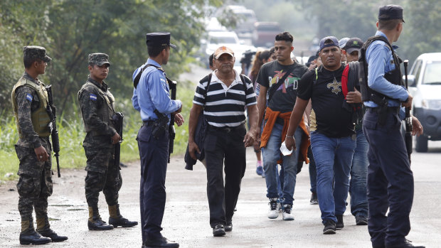 US-bound migrants walk past security forces who are stopping some vehicles carrying migrants to check their documents in Cofradia, Honduras, on Tuesday.
