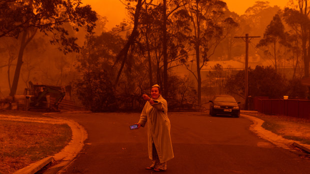 A resident of Mogo, on the NSW south coast, outside her neighbours' property after fire engulfed the town.