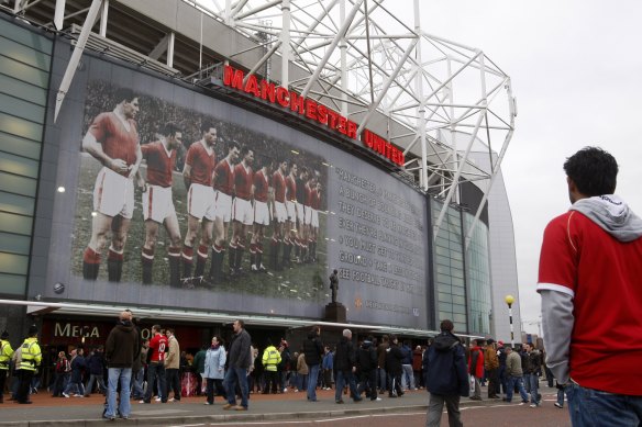 Fans walk past a poster of the Busby Babes on the front of Manchester United’s Old Trafford Stadium.