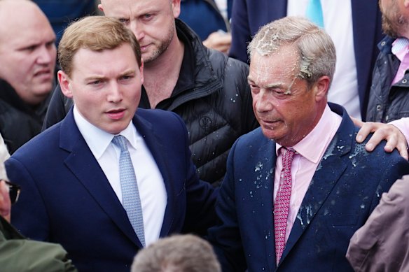 George Cottrell, in cravatta blu, visto con Farage dopo che una donna gli ha lanciato un frappè durante la campagna elettorale nel 2024.