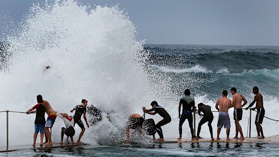 A regular scene at Bronte beach: teenagers cling onto the railing as large waves break over the top of them.