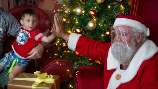 No lap: A child “touches” Santa’s hand  through a plastic shield in a shopping centre in Johannesburg, South Africa.