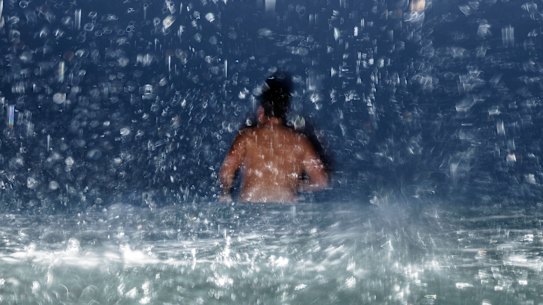 A swimmer takes to the water at Bondi as a downpour sweeps across the beach. 