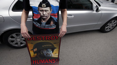 A man wearing a shirt showing a picture of Russian President Vladimir Putin holds an anti NATO poster during a protest outside the Syrian embassy in Belgrade, Serbia, on Sunday.