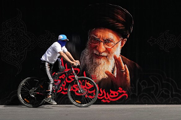 A man rides a bicycle past a portrait of Khamenei in Tehran.