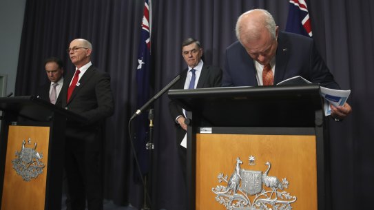 Greg Hunt, Professor Paul Kelly and Professor Brendan Murphy with Prime Minister Scott Morrison taking a closer look at his notes during a press conference on Thursday night.