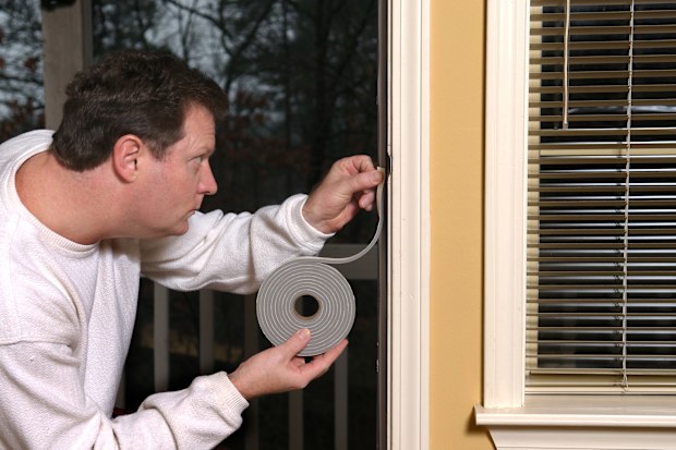 Homeowner applying weather stripping to stop air leaks around a doorway