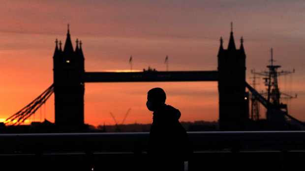 A person wearing a face mask walks across London Bridge, with Tower Bridge in the background.