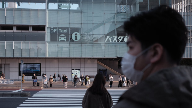 Pedestrians wearing protective masks wait for traffic lights to change near a bus terminal in the Shinjuku district of Tokyo yesterday.