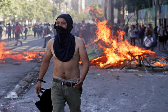 A masked protester walks near a burning barricade during clashes with police in Santiago.