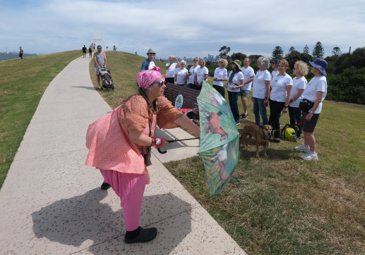 Passerby Samantha Taplin, of Elwood, dances as Elwood Community Choir sings at the Elwood Singing Walking Trail stop 6 near Point Ormond and the beach, with Melbourne CBD in the background.