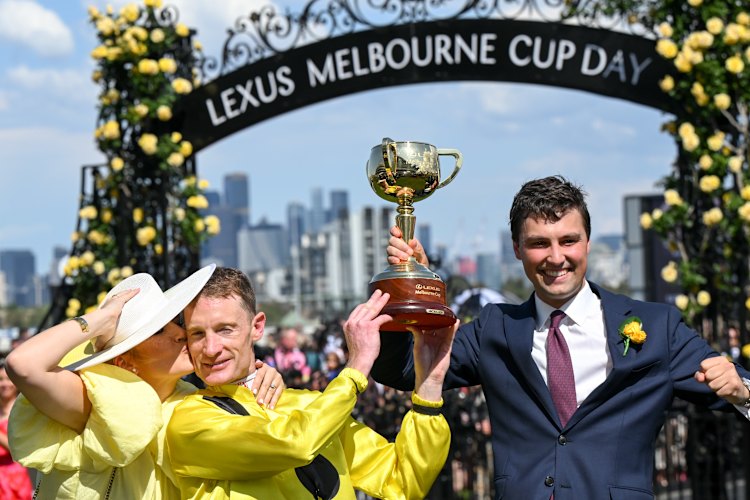 Mark Zahra gets a kiss from wife Elyse after winning the Melbourne Cup as he lifts the trophy with trainer Sam Freedman.