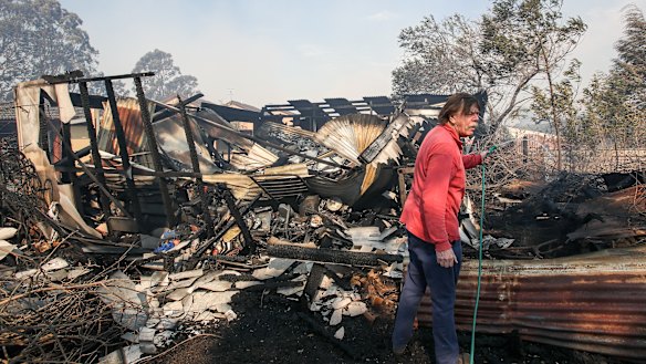 A resident hoses down a shed destroyed by the fire at Bomaderry. 
