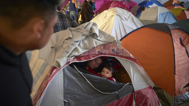 Ruth Aracely Monroy, centre, looks out of the family's tent alongside her 10-month-old son, Joshua, as her husband, Juan Carlos Perla, left, passes inside a shelter for migrants in Tijuana, Mexico. After fleeing violence in El Salvador and requesting asylum in the United States, the family was returned to Tijuana to await their hearing in San Diego last year.
