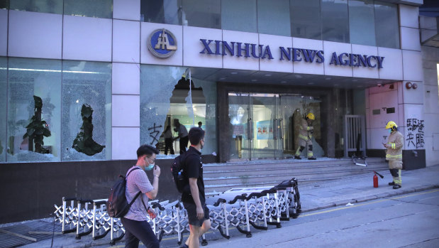 People walk past the offices of China's Xinhua News Agency after its windows were shattered.