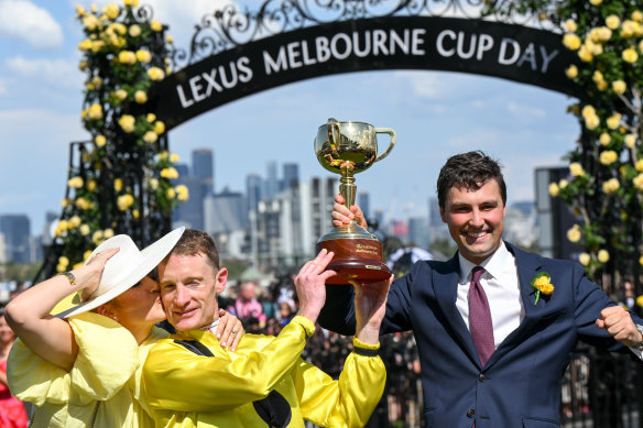 Mark Zahra gets a kiss from wife Elyse after winning the Melbourne Cup as he lifts the trophy with trainer Sam Freedman.