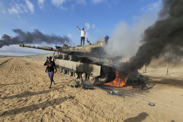 Palestinians celebrate by a destroyed Israeli tank at the Gaza Strip fence east of Khan Younis on October 7.