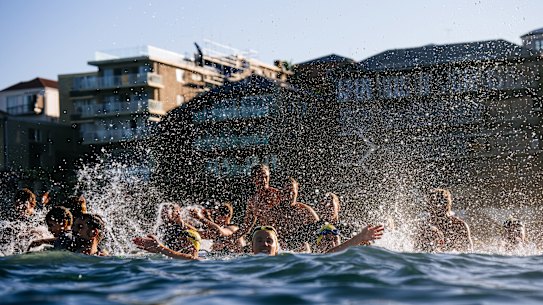 Swimmers and surfers paddle and splash in the ocean and cheer.