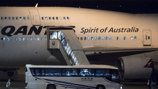 A Japanese worker wearing a protective suit stands next to a bus carrying Australians before boarding the Qantas plane for Darwin. 