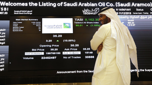 A Saudi stock market official smiles as he watches the stock market screen displaying Saudi Arabia's state-owned oil company Aramco after its trading debut. 