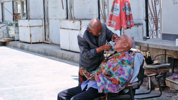 A street barber trims the beard of a man in the streets of Kashgar.