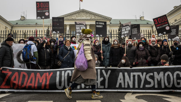 A pedestrian wearing a filter mask passes by demonstrators protesting in the Polish capital Warsaw against what they consider governmental inaction in face of high levels of smog.