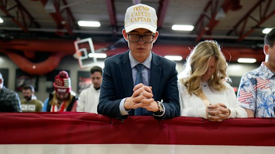 Supporters bow their heads in prayer before a former President Donald Trump commit to caucus rally in Clinton, Iowa.