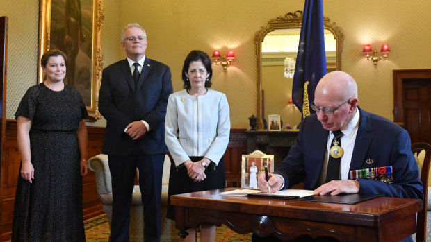 Governor-General David Hurley signs a condolence book as his wife Linda Hurley, Prime Minister Scott Morrison and his wife Jenny Morrison watch on.