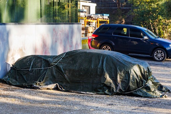 A burnt car was covered by a tarpaulin after the early-morning attack at Lovitt Industries on July 5.