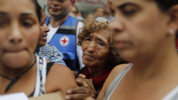 People wait to be given empty water containers and water purification pills during the first aid shipment from the Red Cross in Caracas.