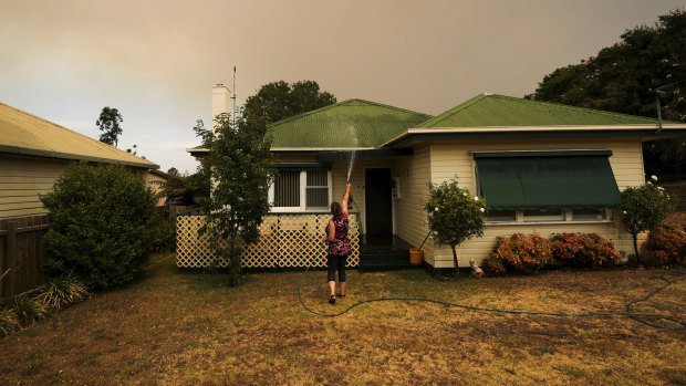 Bruthen resident Janine Pratt hoses down her home as burnt leaves fall on the property.