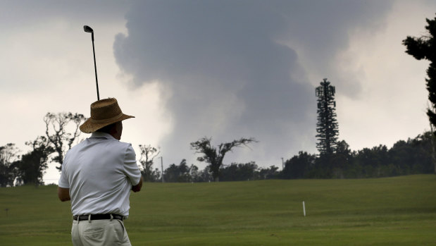 A golfer watches an ash plume rise from the summit of Kilauea volcano on Wednesday.