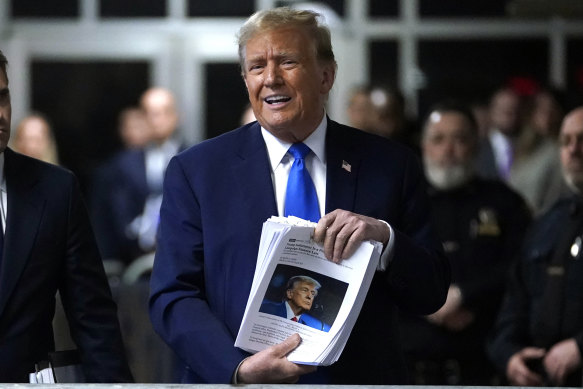 Former president Donald Trump speaks to the media outside court while holding news clippings on Thursday.